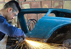 Sparks fly as student grinds on car body.
